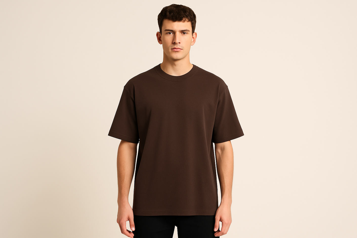 Professional e-commerce product photography of a male model wearing an oversized dark brown crew neck t-shirt, standing straight facing camera with hands relaxed at sides, wearing dark pants against a neutral beige background with studio lighting