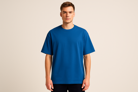 Professional e-commerce product photography of a male model wearing an oversized royal blue crew neck t-shirt, standing straight facing camera with hands relaxed at sides, wearing dark pants against a neutral beige background with studio lighting